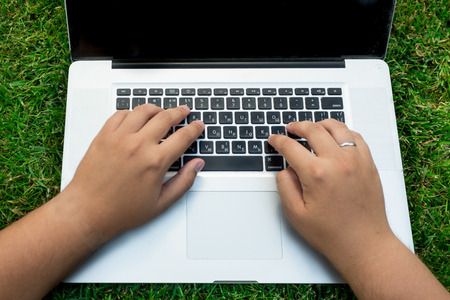 Closeup photo of man using laptop on green grassの写真素材