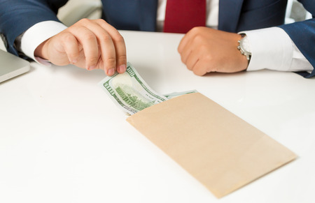 Closeup photo of businessman pulling banknote out of envelope lying on tableの写真素材