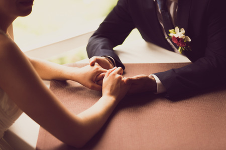Closeup toned photo of bride and groom holding hands at restaurantの写真素材