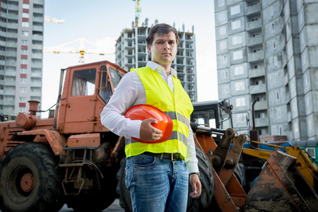Portrait of construction inspector posing next to excavator on building site