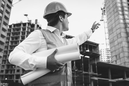 Black and white closeup photo of engineer with blueprints checking building site constructionの写真素材