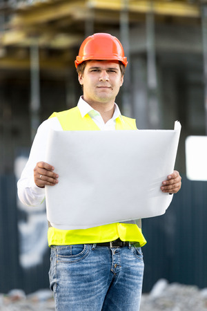 Portrait of foreman in hardhat reading blueprints on building siteの写真素材