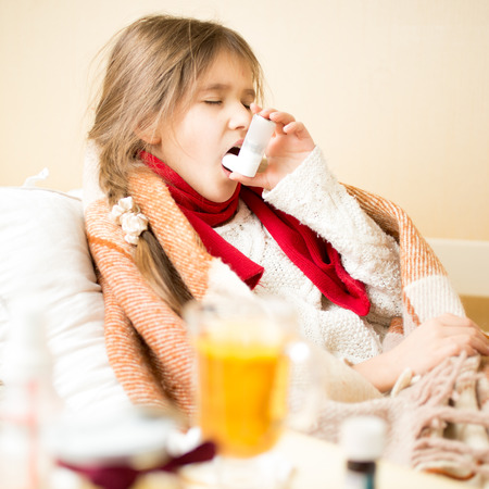 Portrait of sick girl with respiratory illness lying in bed and using inhalerの写真素材