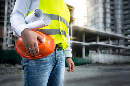 Closeup photo of engineer with hardhat and blueprints posing on building siteの写真素材