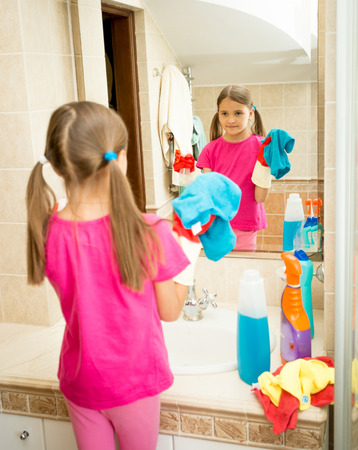Portrait of cute girl cleaning and polishing mirror at bathroomの写真素材