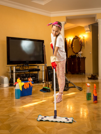 Full length portrait of teenager girl washing wooden floor with swabの写真素材