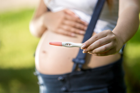 Closeup photo of pregnant woman holding positive pregnancy test