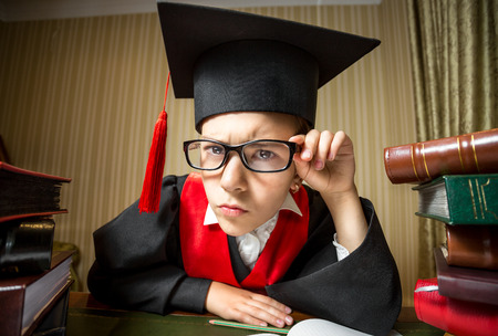 Closeup funny portrait of smart girl in graduation cap and eyeglasses looking at cameraの写真素材