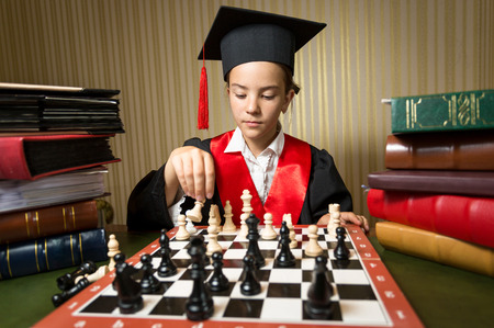 Closeup portrait of smart girl in graduation cap playing chessの写真素材
