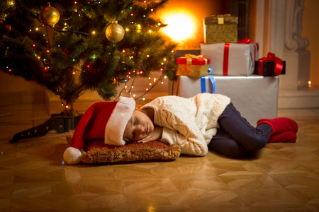 Cute girl fell asleep under Christmas tree while waiting for Santaの写真素材