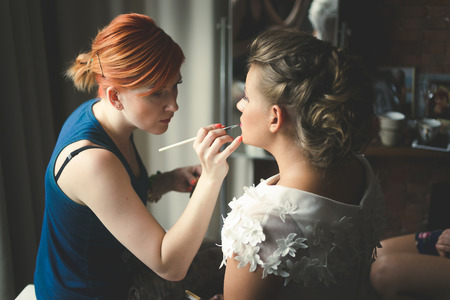 Toned portrait of makeup artist preparing blonde bride at morningの写真素材