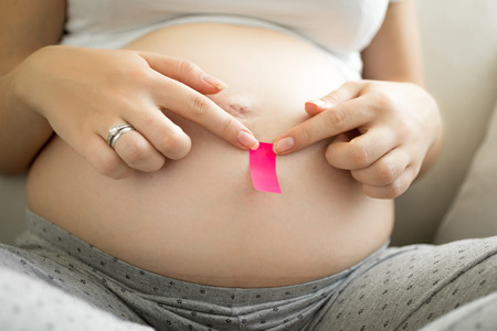 Young pregnant woman sticking pink memo sticker on bellyの写真素材