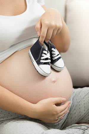 Pregnant woman holding baby boy shoes on belly