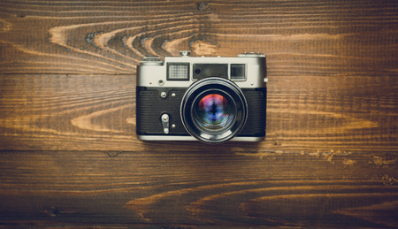 Toned image of old analog camera with manual lens on wooden background