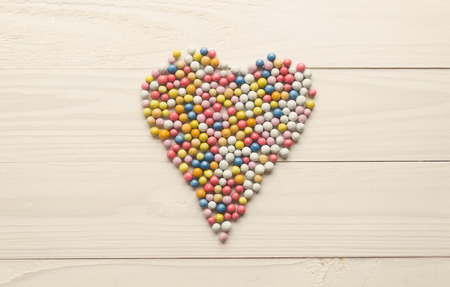 Toned image of colorful round candies lying in shape of heart on white wooden backgroundの写真素材