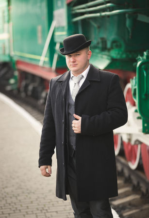 Toned portrait of handsome man in suit and bowler hat waiting for trainの写真素材