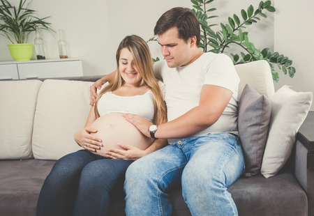 Toned photo of happy couple expecting baby relaxing on sofaの写真素材