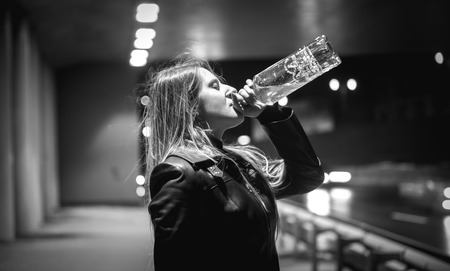 Closeup black and white portrait of woman drinking whiskey at night on streetの写真素材