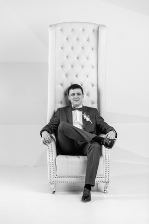 Black and white portrait of handsome stylish man posing at studio in armchairの写真素材