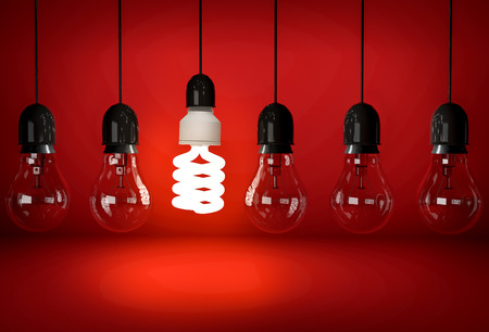 Glowing eco saving bulb hanging on wire in row of incandescent bulbs over red backgroundの写真素材