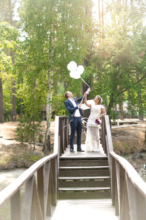 Beautiful just married couple holding white balloons on wooden bridgeの写真素材