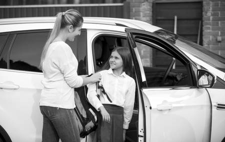 Black and white portrait of schoolgirl getting into the car and giving bag to motherの写真素材