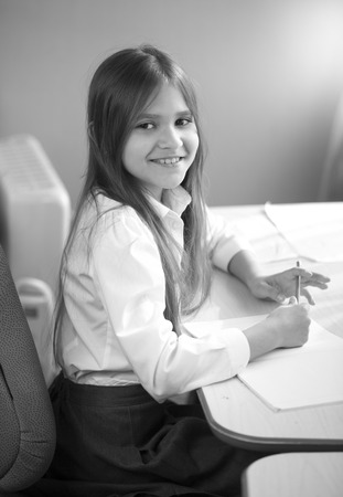 Black and white portrait of cute smiling schoolgirl posing behind desk at bedroomの写真素材