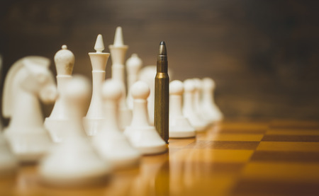Closeup toned photo of bullet in row of white chess pieces on wooden boardの写真素材