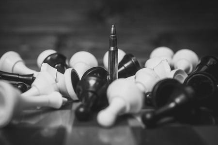 Black and white conceptual photo of bullet among lying down chess piecesの写真素材