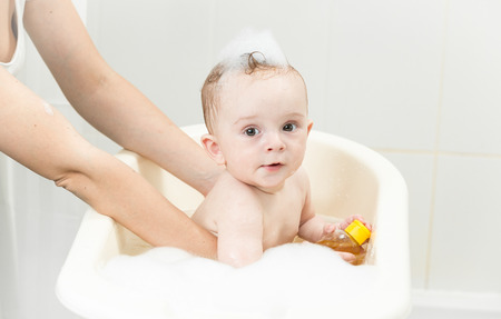 Young mother bathing her baby boy in plastic bathの写真素材