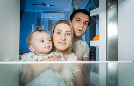 Portrait of family in pajamas looking inside the refrigerator for something to eatの写真素材