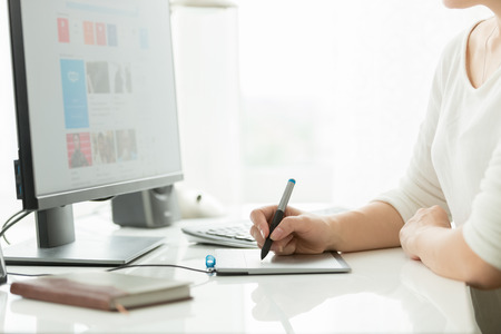 Young female designer using digital graphic tablet while working on computer