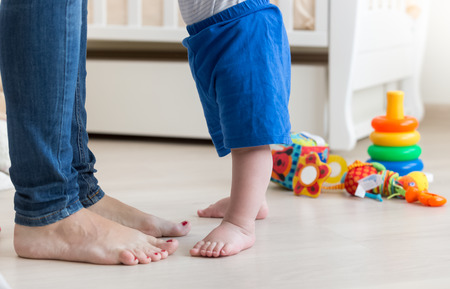 Closeup photo of small baby's feet on floor at living room next to mothers feetの写真素材