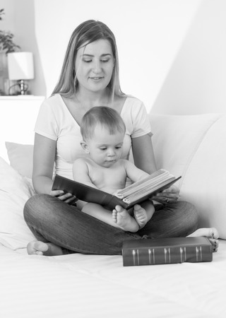 Black and white portrait of smiling young mother reading book to her babyの写真素材
