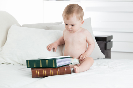 Adorable baby boy using digital table lying on stack of books. Concept of baby educationの写真素材