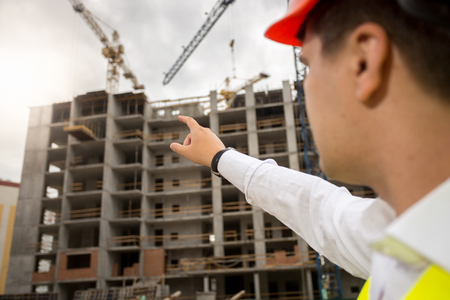 Closeup image of construction engineer pointing with hand at building under constructionの写真素材