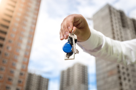 Closeup photo of male hand holding keys from new home on background of buildings under constructionの写真素材