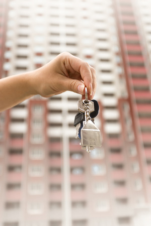 Closeup image of hand holding keys against high new buildingの写真素材