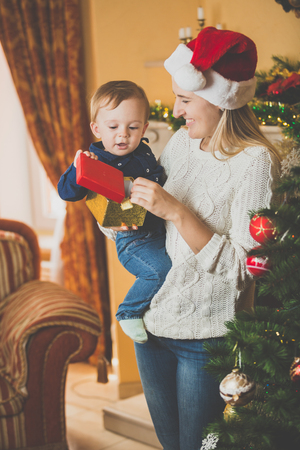 Toned portrait of happy young mother giving Christmas present to her cute baby boy at living roomの写真素材