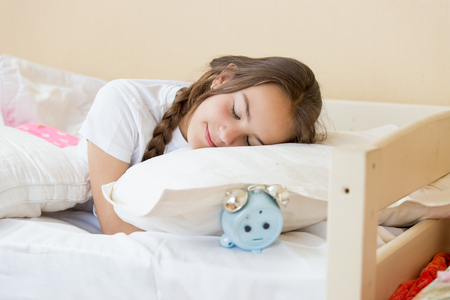 Portrait of beautiful brunette teenage girl sleeping on alarm clock the pillowの写真素材