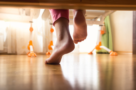 Closeup photo of female feet under the bed on wooden floorの写真素材