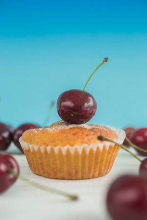 Macro photo of tasty muffin with fresh cherry on top over blue backgroundの写真素材