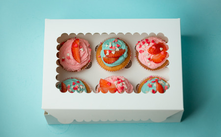 Closeup photo of six colorful cupcakes decorated with sprinkles and strawberries in closed paper boxの写真素材