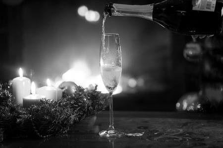 Closeup black and white image of champagne flute being filled from bottle in living room on Christmas eveの写真素材