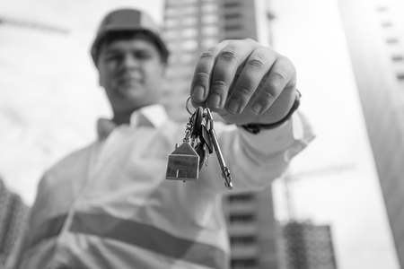 Black and white closeup photo of young architect holding keys from new home on hand