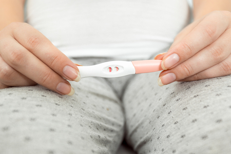 Conceptual photo of woman holding positive pregnancy test at bathroomの写真素材