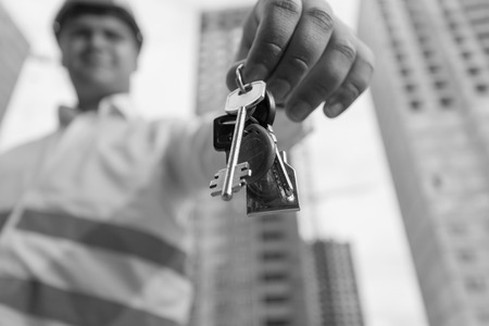 Black and white portrait of young smiling construction engineer holding keys from new home....