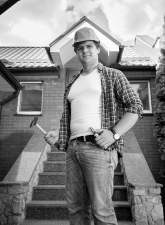 Black and white portrait of smiling construction worker posing in front of finished house
