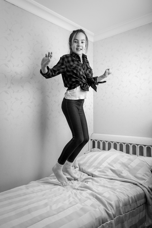 Black and white cheerful teenage girl jumping high in her bedの写真素材