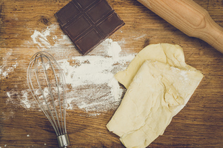 Rolling pin, chocolate, flour and dough lying on wooden boardの写真素材